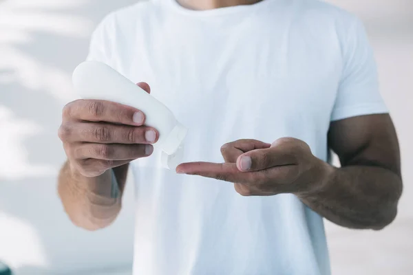 Обрізаний вид людини, що кладе косметичний крем на палець з білої пляшки — стокове фото