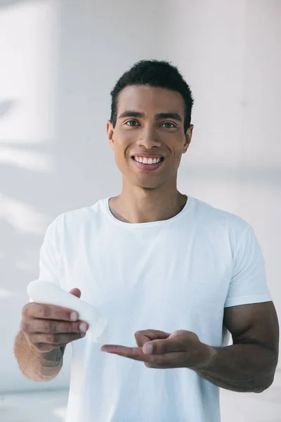Handsome young man putting cosmetic cream on finger from white bottle — Stock Photo