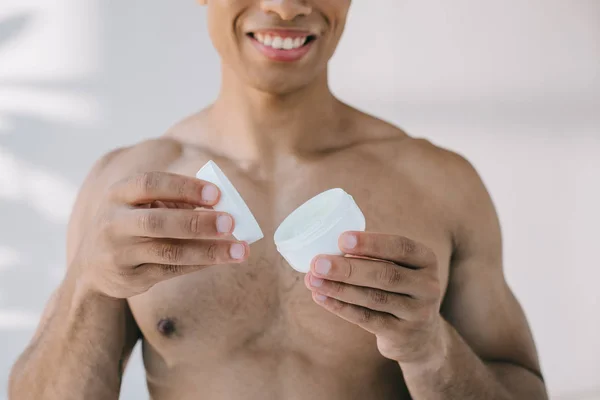 Vista cortada de bonito misto raça homem abertura recipiente com creme cosmético — Fotografia de Stock