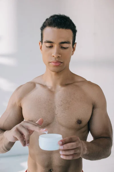 Serious mixed race man taking some cosmetic cream from container — Stock Photo