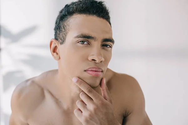 Serious mixed race man looking at camera while touching chin — Stock Photo
