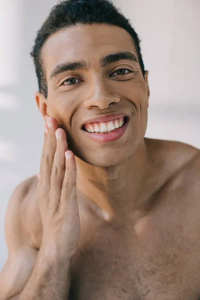 Portrait shot of muscular mixed race man touching cheek while smiling and looking at camera — Stock Photo