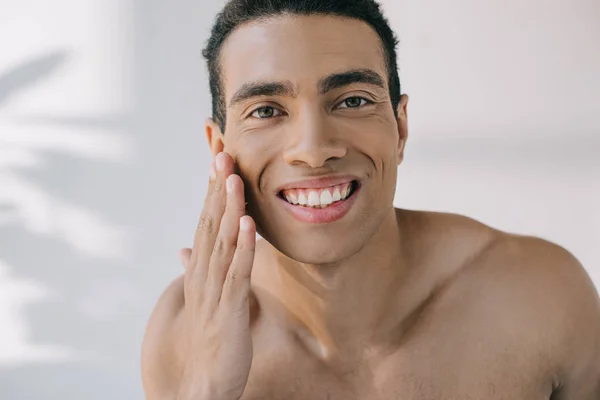 Retrato tiro de bonito misto raça homem tocando bochecha enquanto sorrindo e olhando para a câmera — Fotografia de Stock