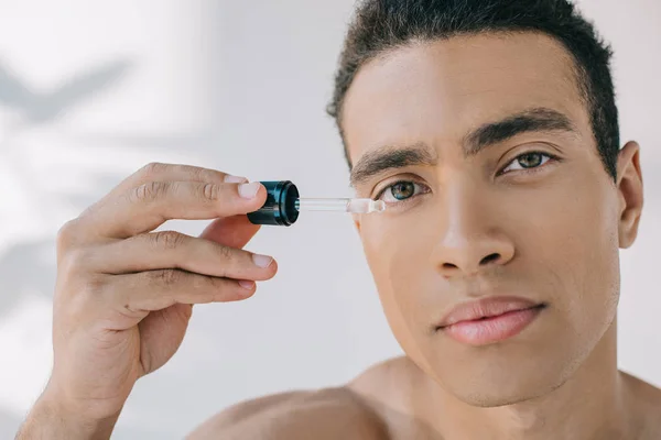 Portrair shot of mixed race man holsing pipette with serum and looking at camera — Stock Photo