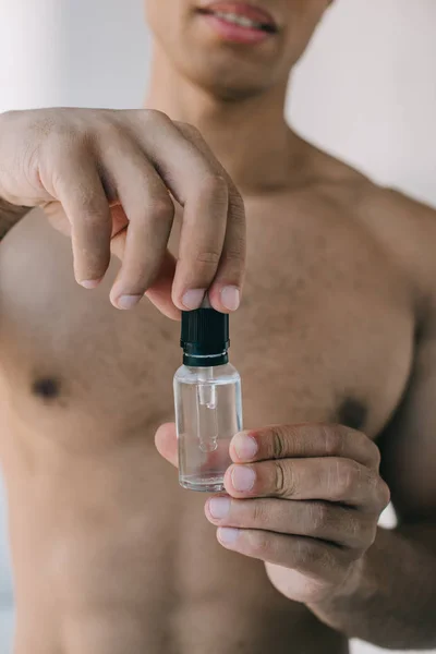 Вибірковий фокус м'язової змішаної раси чоловік відкриває пляшку з косметичною сироваткою — стокове фото