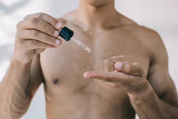 Selective focus of mixed race man dropping serum from pipette on finger — Stock Photo