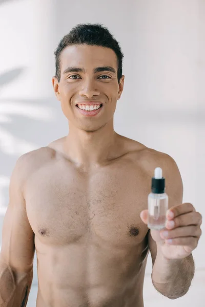 Handsome muscular man showing bottle with serum and looking at camera — Stock Photo