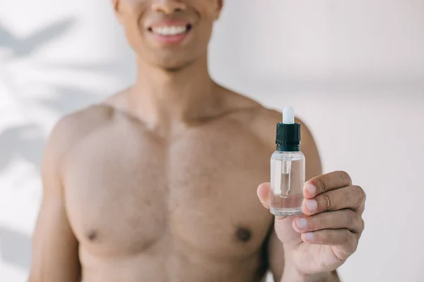 Селективный фокус мускулистого человека смешанной расы, показывающего бутылку с сывороткой на камеру — стоковое фото