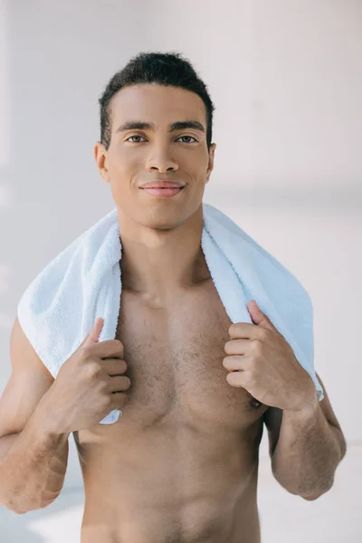 Musculoso hombre de raza mixta sosteniendo toalla azul en los hombros y mirando a la cámara - foto de stock