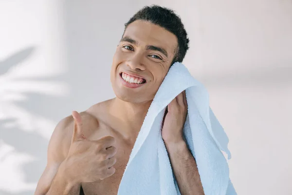 Muskulöser Mischlingsmann wischt Gesicht mit blauem Handtuch ab, zeigt Daumen hoch, lächelt und blickt in die Kamera — Stockfoto