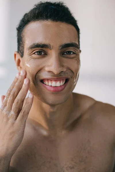 Retrato de un joven con la cara mojada tocándolo con la mano mientras sonríe y mira a la cámara - foto de stock