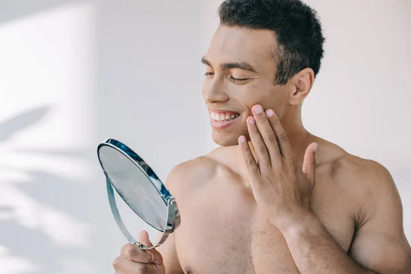Handsome mixed race man touching face with hand while looking at mirror — Stock Photo