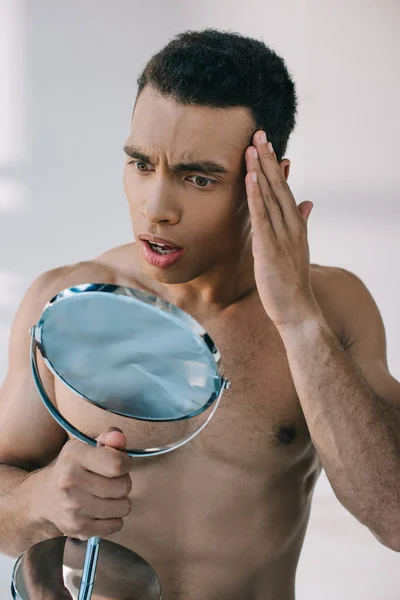 Shoked handsome mixed race man touching temple with hand and looking at mirror — Stock Photo