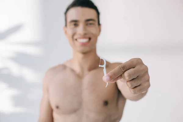 Вибірковий фокус змішаної раси людини, що представляє зубну нитку на паличці і посміхається на камеру — стокове фото