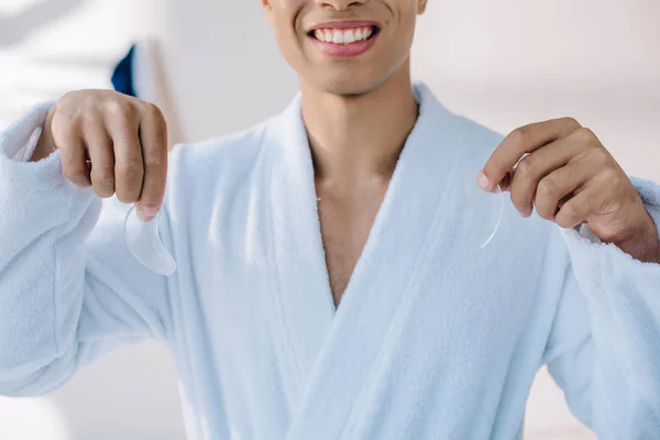 Cropped view of man in bathrobe holding patches for eye bags — Stock Photo