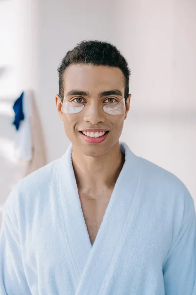 Hombre guapo en albornoz con parches sonriendo y mirando a la cámara - foto de stock