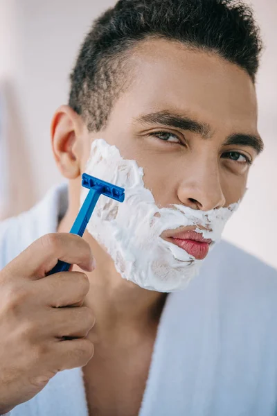 Retrato de hombre guapo afeitándose la cara con afeitadora y mirando a la cámara - foto de stock