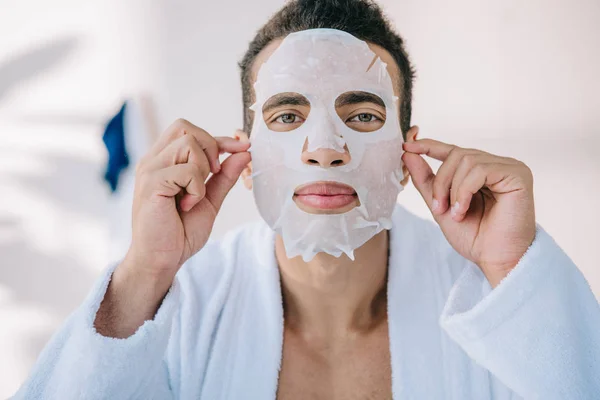 Mann mit Gesichtsmaske im Bademantel blickt in Kamera — Stockfoto