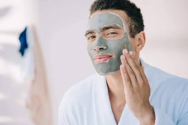 Young man applying face mask with hand and looking at camera — Stock Photo