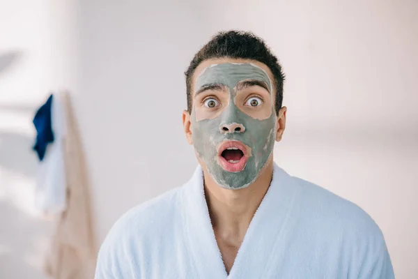 Shocked man with clay mask on face looking at camera — Stock Photo