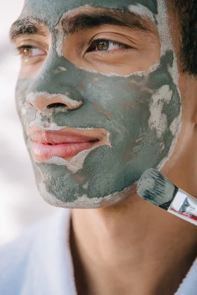 Close up view of handsome man applying face mask with brush and looking away — Stock Photo