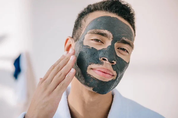 Selbstbewusster junger Mann trägt Gesichtsmaske mit der Hand auf und blickt in die Kamera — Stockfoto