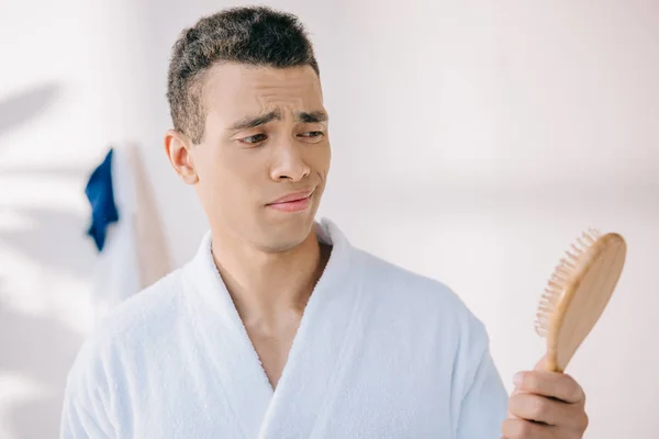 Disappointed young man in bathrobe holding hairbrush — Stock Photo