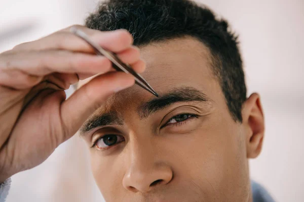 Vue rapprochée du jeune homme arrachant les sourcils avec une pince à épiler — Photo de stock