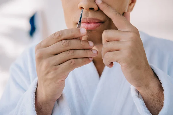 Cropped view of young man plucking nose with tweezer — Stock Photo
