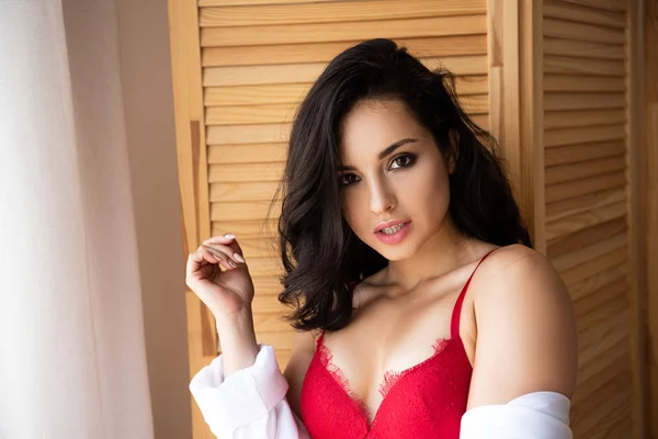 Fille sexy en sous-vêtements rouges et chemise blanche debout près du diviseur de pièce en bois et regardant la caméra — Photo de stock