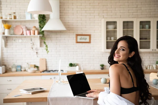 Menina sexy em roupa interior preta e camisa branca usando laptop, sorrindo e olhando para a câmera — Fotografia de Stock