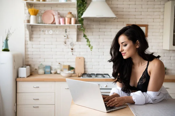 Chica sexy en ropa interior negro usando el ordenador portátil, mientras que de pie en la cocina - foto de stock