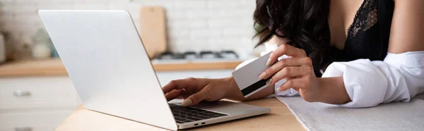 Tiro panorâmico de menina em roupa interior preta e camisa branca usando laptop e segurando cartão de crédito — Fotografia de Stock