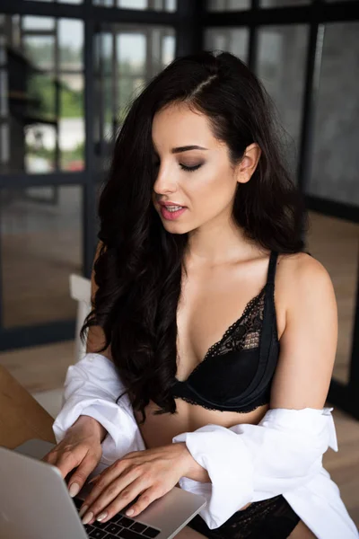 Sexy girl in black underwear and white shirt using laptop with closed eyes — Stock Photo
