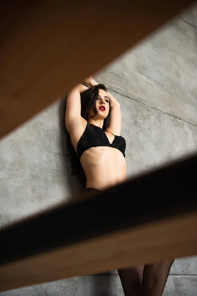 Selektiver Fokus des sexy Mädchens in schwarzer Unterwäsche, das sich an die graue Wand lehnt und wegschaut — Stockfoto