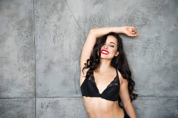 Sexy ragazza in biancheria intima nera appoggiata sulla parete grigia e sorridente con gli occhi chiusi — Foto stock