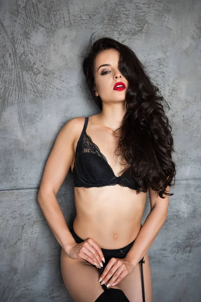 Sexy ragazza in biancheria intima nera appoggiata sulla parete grigia e tenendo calze — Foto stock