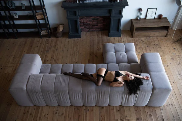 Vista de ángulo alto de chica sexy en ropa interior negro posando con los ojos cerrados mientras está acostado en el sofá en la sala de estar - foto de stock