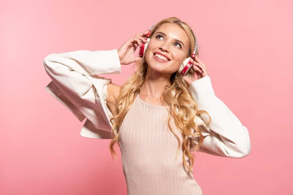 Belle blonde rêveuse femme heureuse écoutant de la musique dans des écouteurs isolés sur rose — Photo de stock