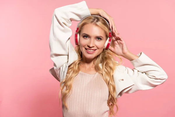 Красива блондинка щаслива жінка слухає музику в навушниках ізольована на рожевому — стокове фото