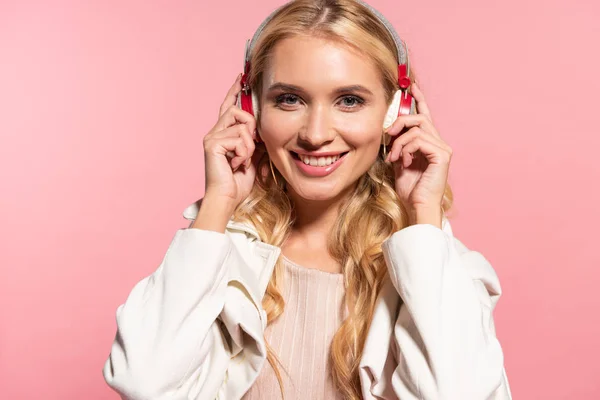 Schöne blonde glückliche Frau hört Musik in Kopfhörern isoliert auf rosa — Stockfoto