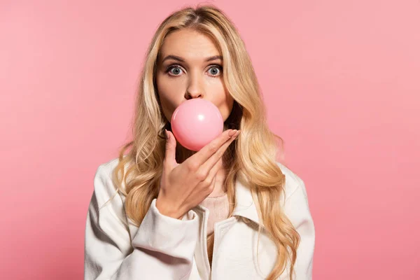 Blonde jeune femme avec rose bulle gomme dans la bouche isolé sur rose — Photo de stock