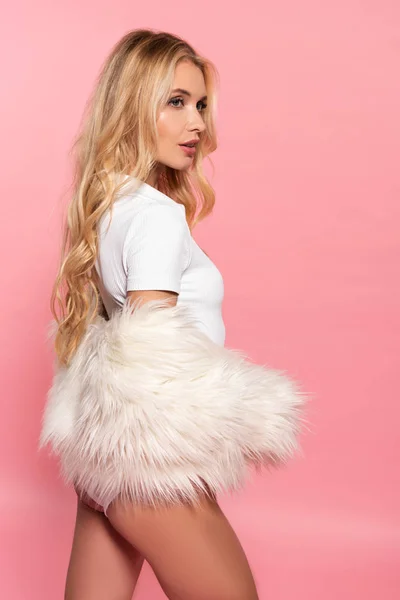 Side view of beautiful sexy blonde woman in white bodysuit and faux fur jacket isolated on pink — Stock Photo