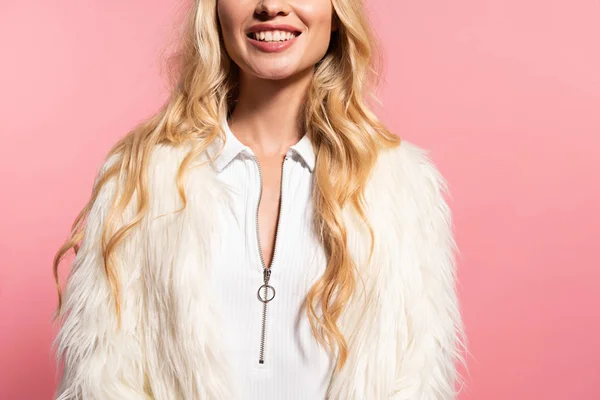 Обрізаний вид щасливої красивої блондинки в білому боді-костюмі і штучному хутряному піджаку ізольовані на рожевому — стокове фото