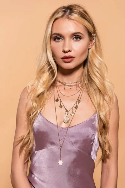 Elegant blonde woman in violet satin dress and necklace isolated on beige — Stock Photo