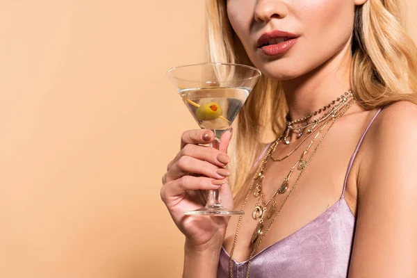 Vista ritagliata di elegante donna bionda in abito di raso viola e collana in possesso di cocktail isolato su beige — Foto stock