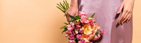 Vista parziale di donna elegante in abito di raso viola con mazzo di fiori isolati su beige, colpo panoramico — Foto stock