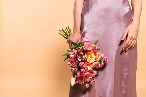 Vista parziale di donna elegante in abito di raso viola con mazzo di fiori isolati su beige — Foto stock