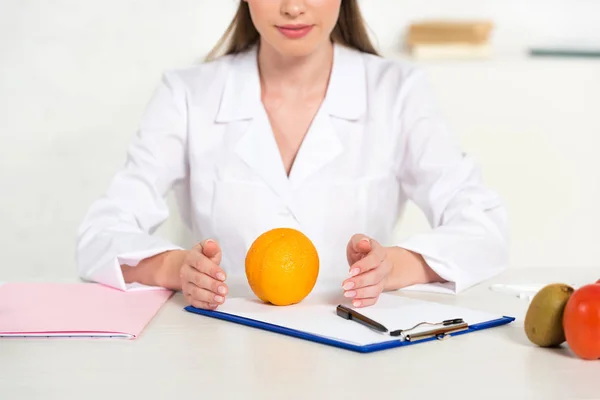 Teilansicht einer Ernährungsberaterin im weißen Kittel mit Obst und Gemüse am Arbeitsplatz — Stockfoto