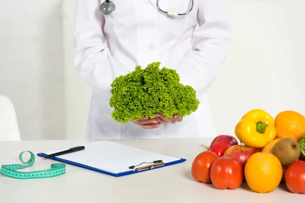 Cropped view of dietitian in white coat holding lettuce at workplace — Stock Photo